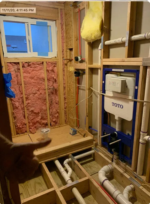 Bathroom plumbing rough-in showing TOTO wall-hung toilet carrier installation with PVC drain lines and copper supply pipes