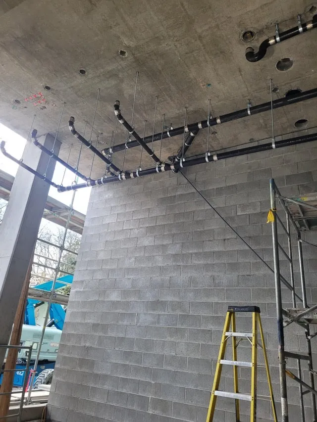 Commercial ceiling-mounted plumbing installation showing industrial pipe network with proper supports and connections