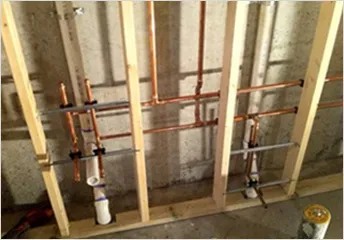 Copper water supply line rough-in behind wall framing showing soldered joints and proper pipe mounting