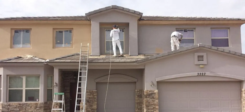 Professional painting crew on ladders spray painting two-story stucco home exterior in Bay Area