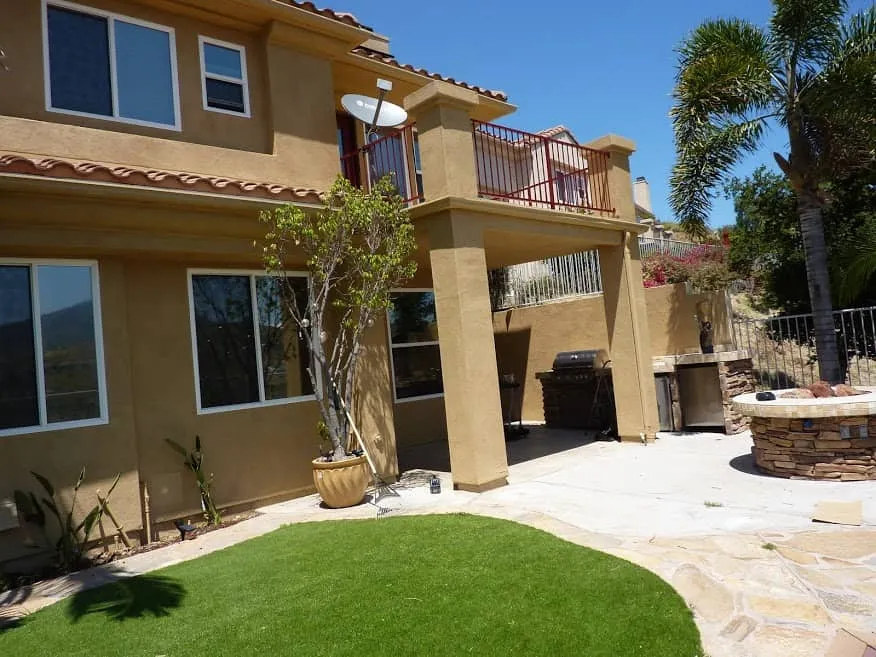 Completed exterior stucco painting rear view showing patio area with outdoor kitchen and artificial turf