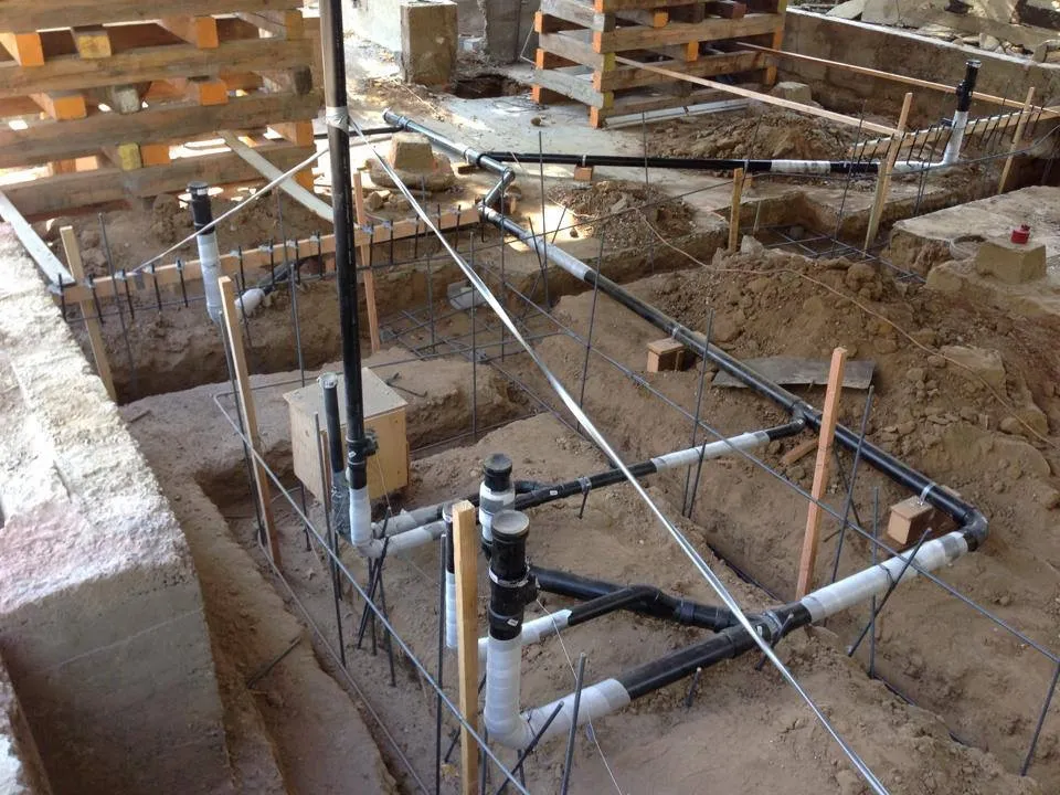 Foundation plumbing rough-in showing PVC drain waste vent pipes laid in trenches with rebar before concrete pour