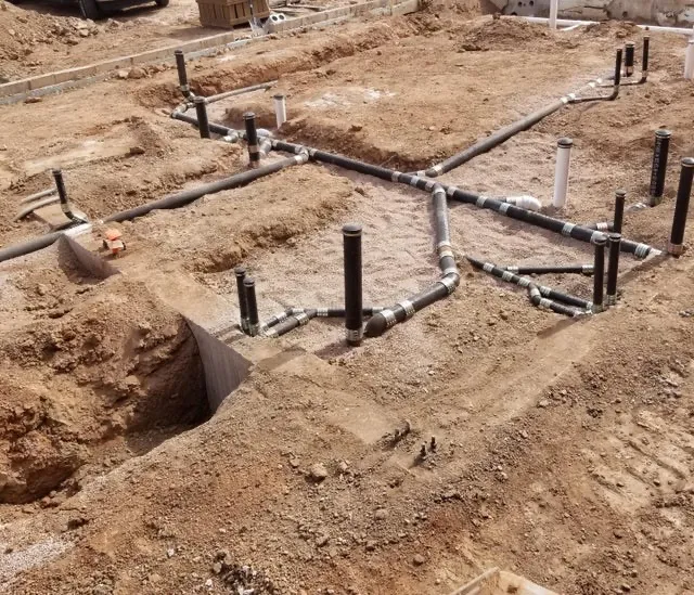 Underground plumbing installation with PVC pipes and clean-outs in foundation trenches ready for inspection